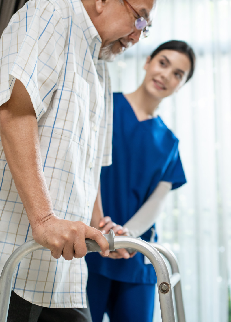 Photo of a man with a walker being assisted by a female provider.